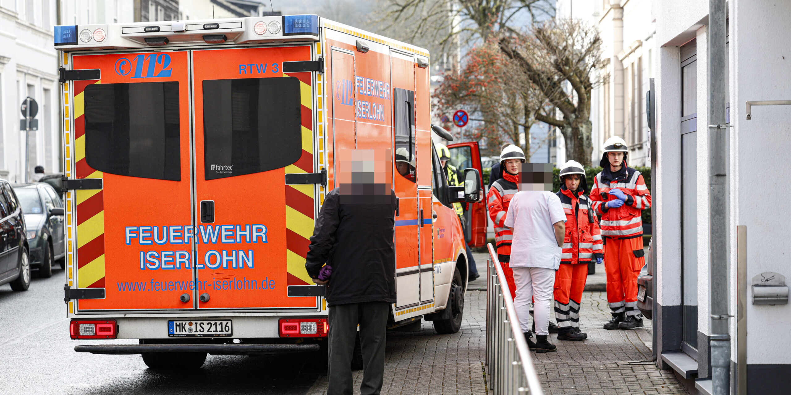 Rettungseinsatz mit Feuerwehr Iserlohn: Sanitäter und Passanten vor einem Einsatzfahrzeug in der Stadt.