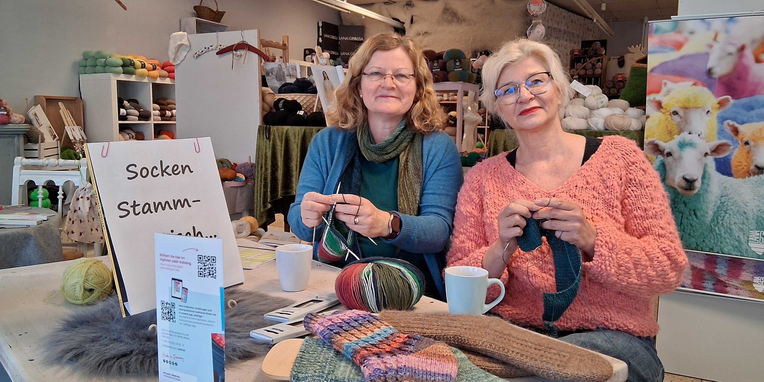 Zwei Frauen stehen in einem Geschäft und sticken mit Wolle.