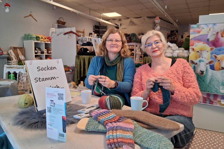 Zwei Frauen stehen in einem Geschäft und sticken mit Wolle.