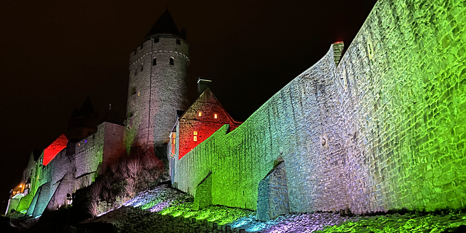 Die Fassade der Burg Altena wird bei Nacht bunt beleuchtet.