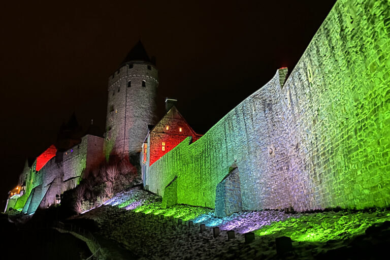 Die Fassade der Burg Altena wird bei Nacht bunt beleuchtet.