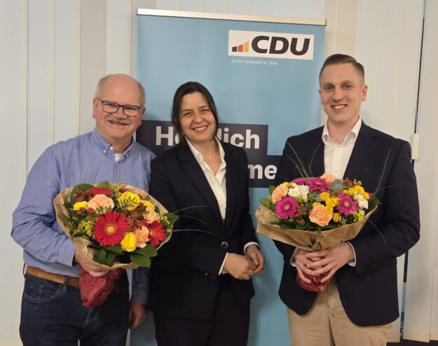 Foto: CDU Altena Politiker stehen vor einem Werbeplakat, zwei Männer halten Blumensträuße in der Hand.