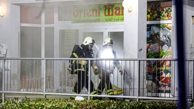 Foto: Dennis Echtermann Zwei Feuerwehrleute laufen aus einem brennenden Supermarkt heraus.