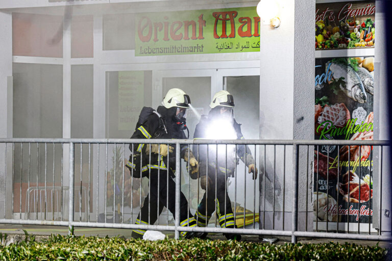 Zwei Feuerwehrleute laufen aus einem brennenden Supermarkt heraus.