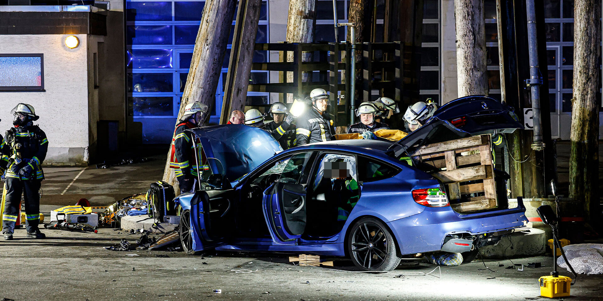 EIn blauer Unfallwagen steht auf einem Bauhof. Feuerwehrleute befreien ein Unfallopfer.