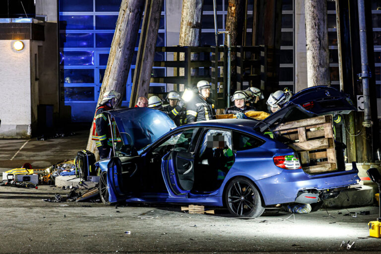 EIn blauer Unfallwagen steht auf einem Bauhof. Feuerwehrleute befreien ein Unfallopfer.