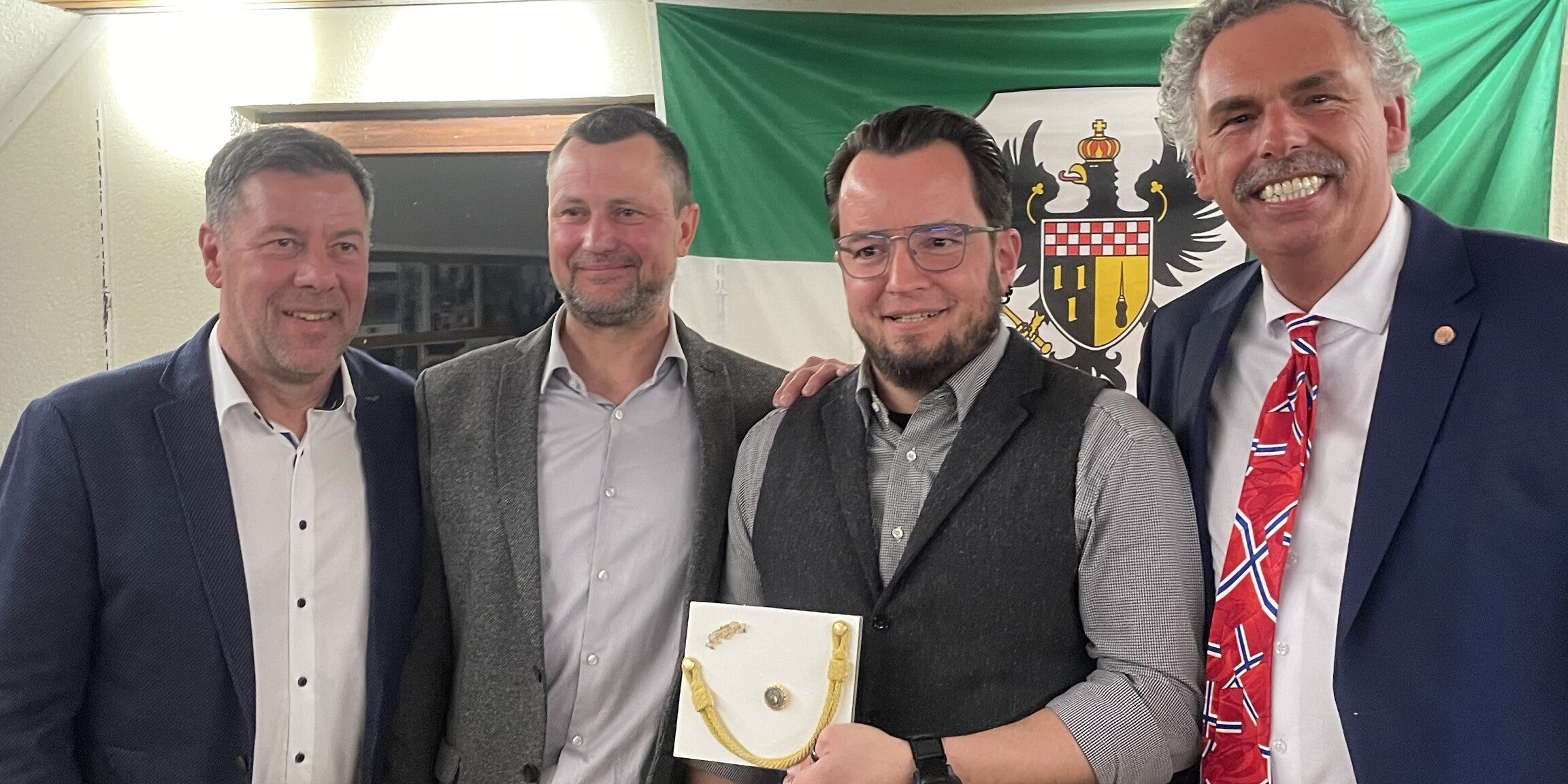 Vier Männer stehen vor einer Schützenfest-Fahne.