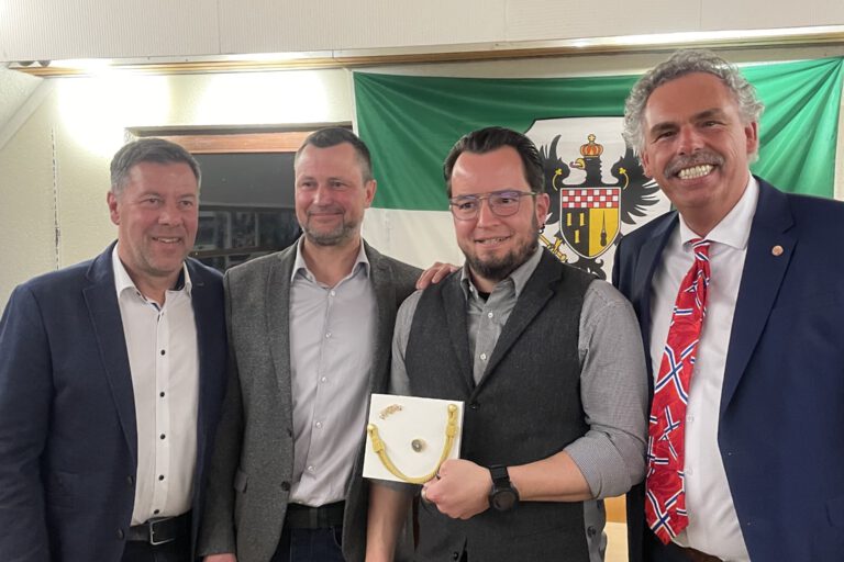 Vier Männer stehen vor einer Schützenfest-Fahne.