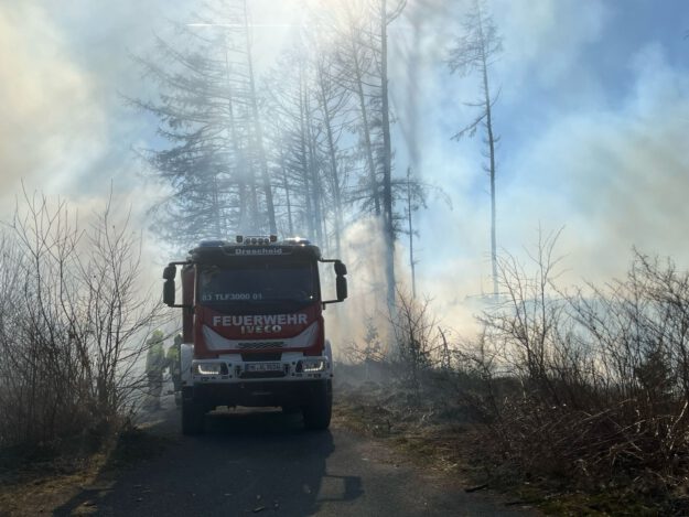 Ein Feuerwehrfahrzeug steht in einem brennenden Wald.