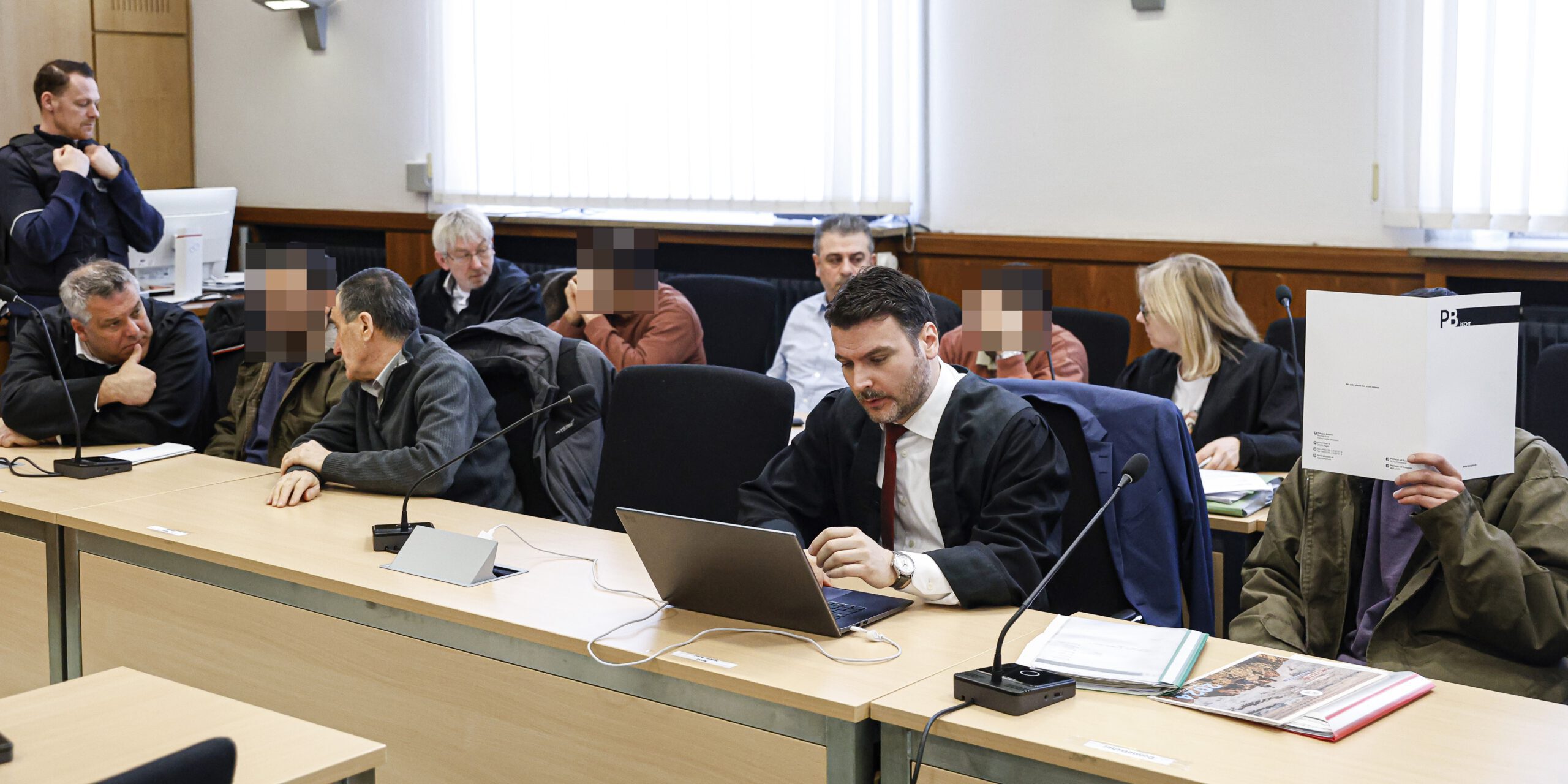 Vier Angeklagte sitzen mit Anwälten in einem Gerichtssaal.