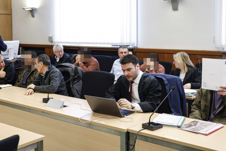 Vier Angeklagte sitzen mit Anwälten in einem Gerichtssaal.