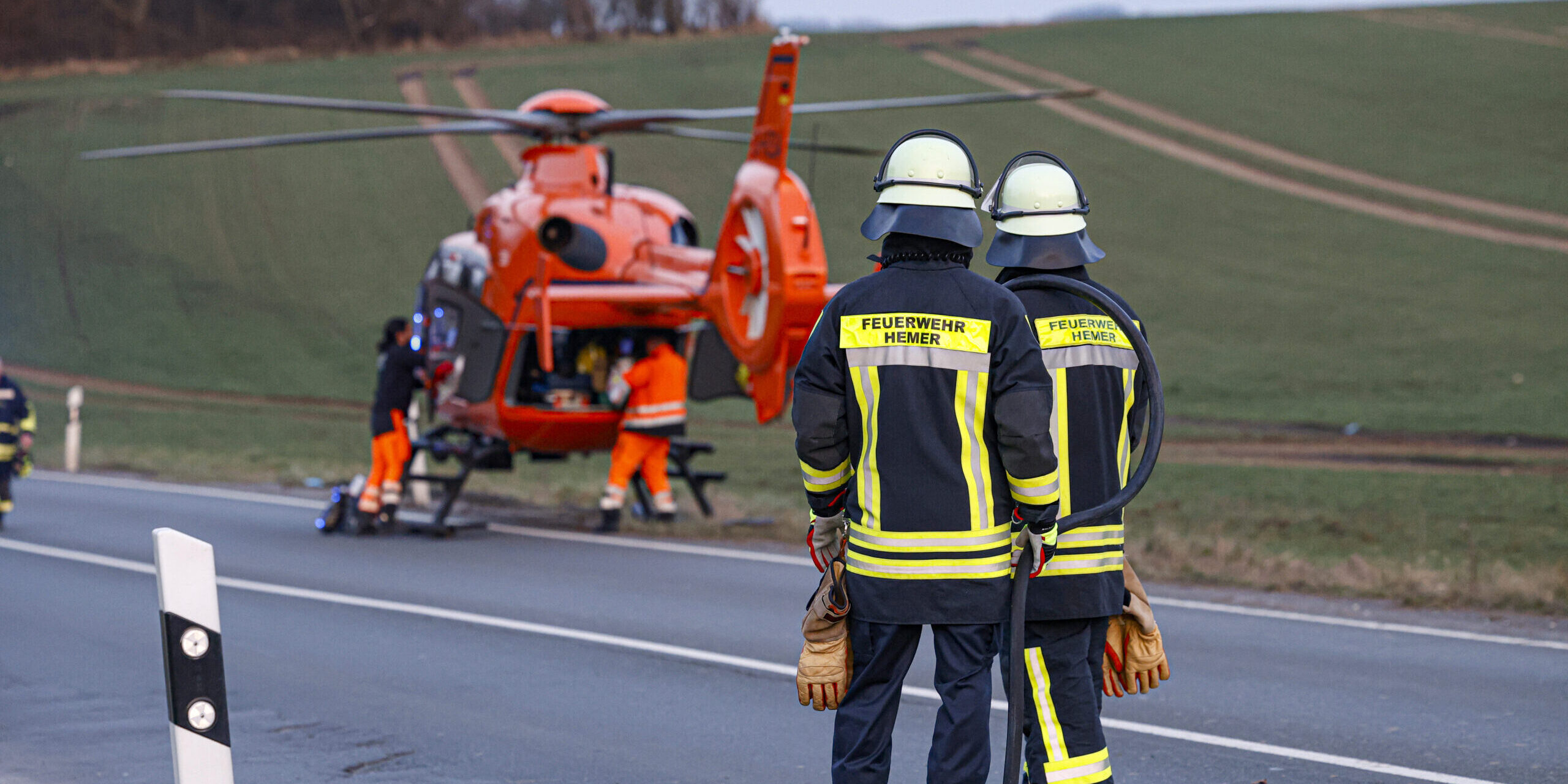 Zwei Feuerwehrmänner stehen vor einem gelandeten Rettungshubschrauber.