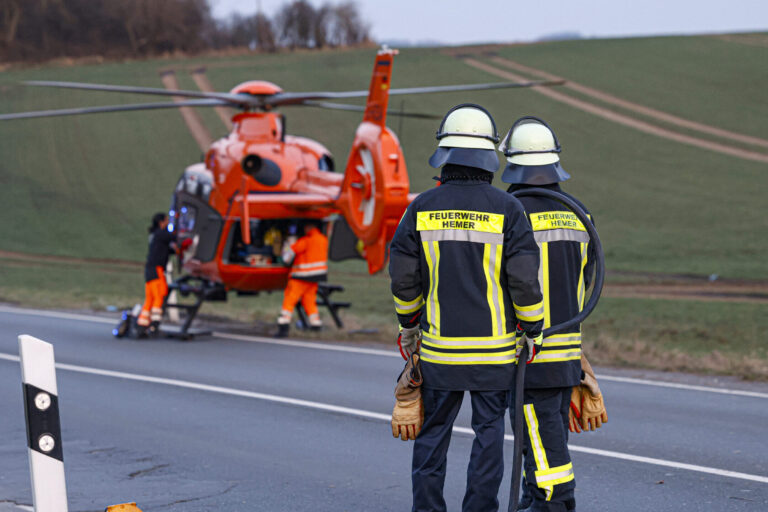 Zwei Feuerwehrmänner stehen vor einem gelandeten Rettungshubschrauber.