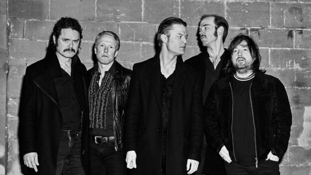 Foto: Daniel Olsen Eine Musikgruppe steht vor einer Wand. Das Bild ist schwarz-weiß.