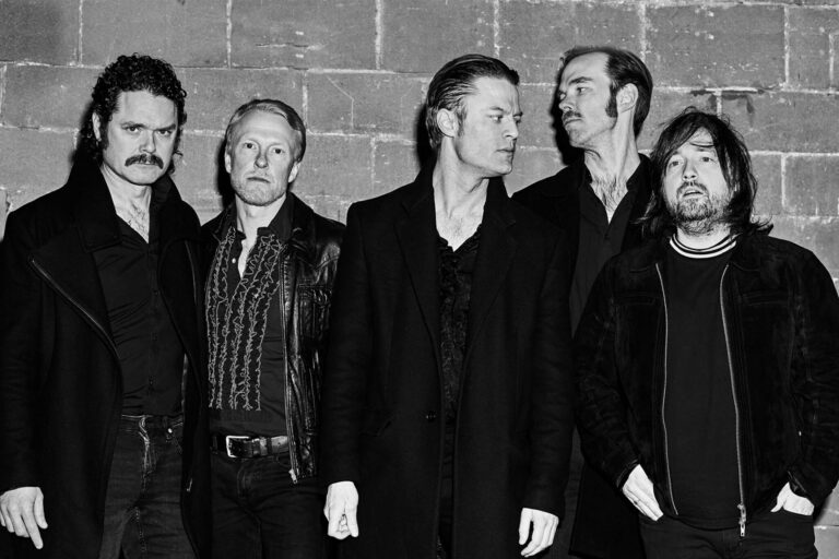 Eine Musikgruppe steht vor einer Wand. Das Bild ist schwarz-weiß.