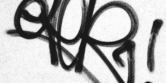 Schwarzes Graffiti auf einer weißen Hauswand.