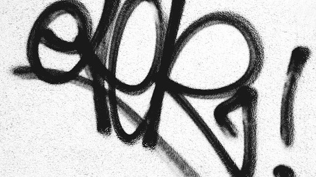 Schwarzes Graffiti auf einer weißen Hauswand.