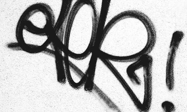 Schwarzes Graffiti auf einer weißen Hauswand.