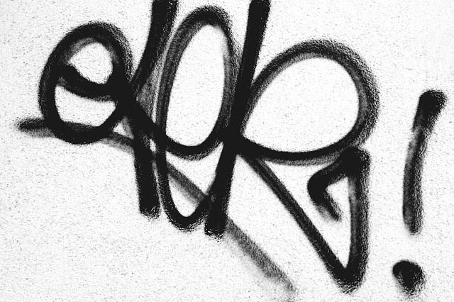 Schwarzes Graffiti auf einer weißen Hauswand.