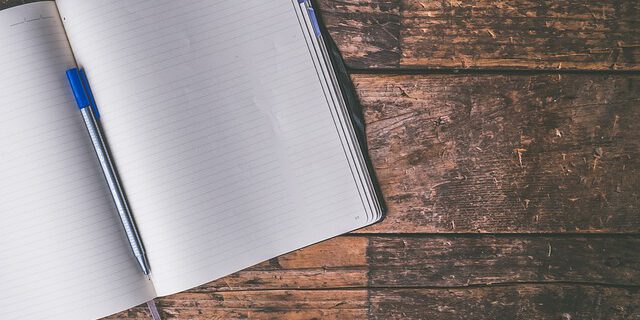 Ein aufgeschlagenes Notizbuch liegt auf einem Holztisch.