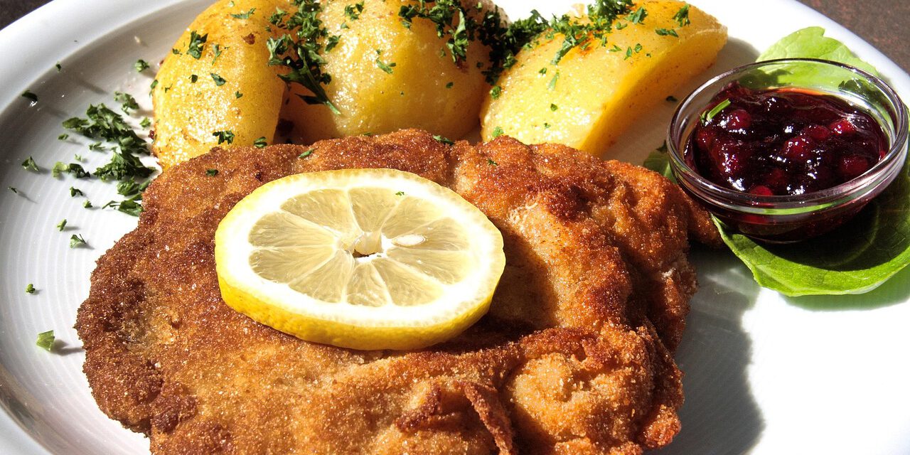 Panierte Schnitzel auf einem weißen Teller, serviert mit Zitronenscheibe und Petersilie, daneben ein kleiner Salat und Kartoffeln.