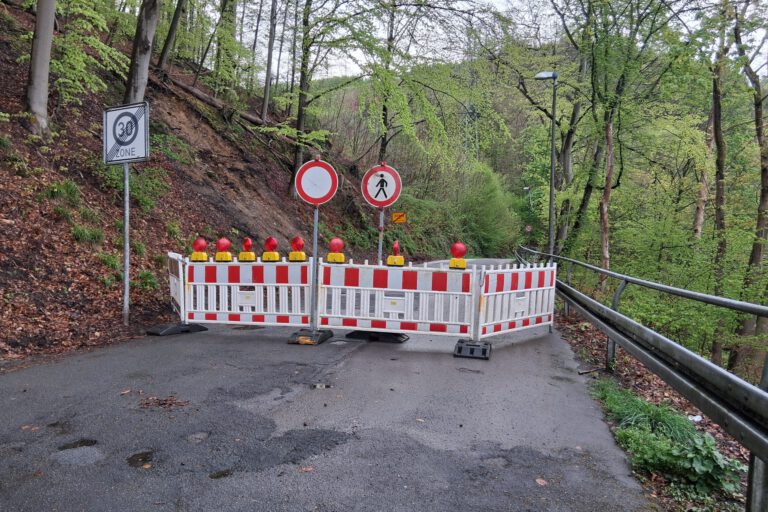 Absperrbaken blockieren eine Straße. Schilder verbieten die Durchfahrt für Autos und Fußgänger.