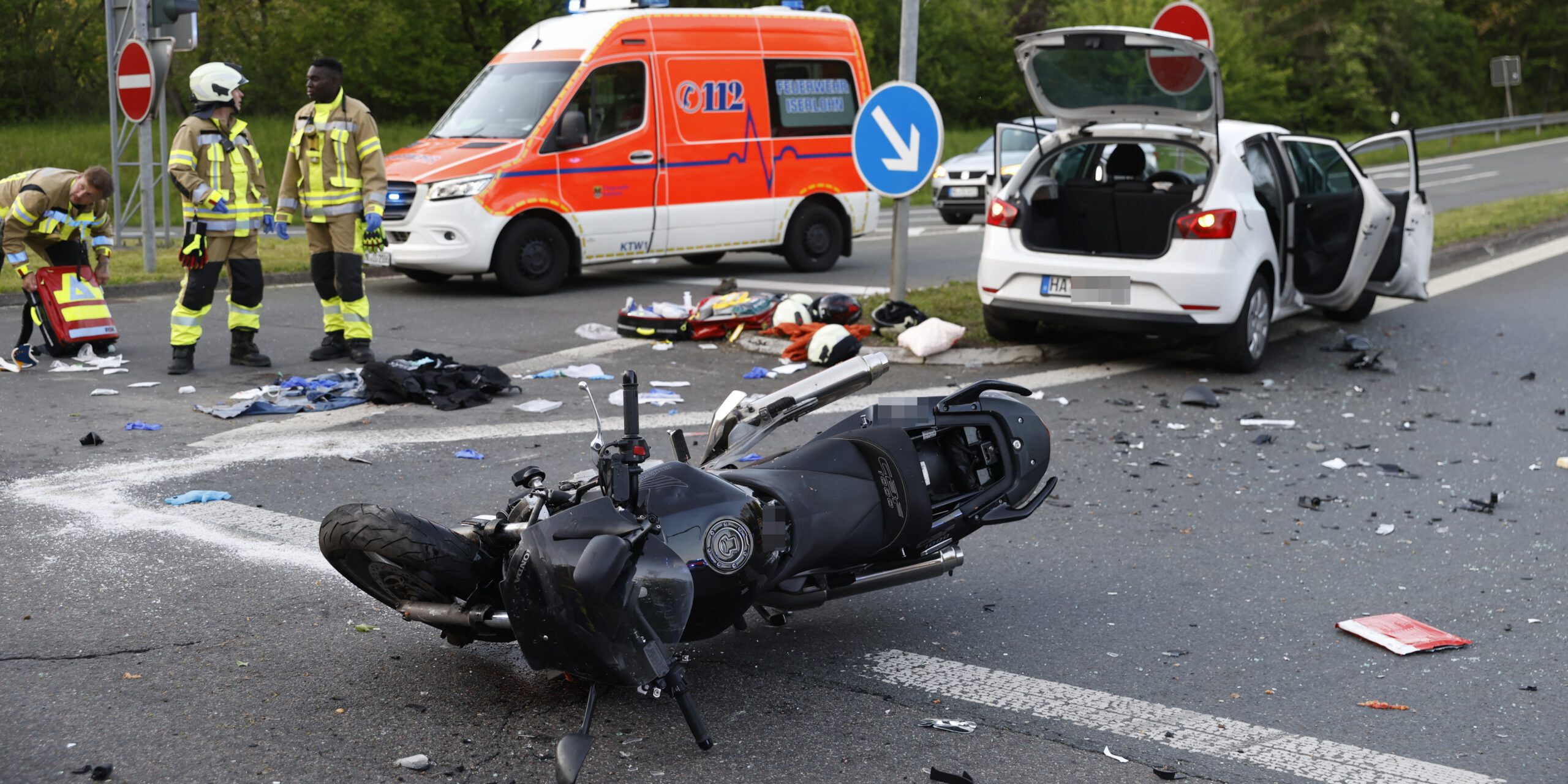 Der Unfallort an der Auffahrt der Anschlussstelle Iserlohn-Seilersee glich einem Trümmerfeld.
© Foto: Dennis Echtermann Das Wrack eines Motorrads liegt nach einem Unfall auf der Straße. Im Hintergrund stehen eine weißer Pkw und ein Notarztfahrzeug. Links am Bildrand drei Rettungskräfte.