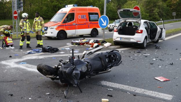 Foto: Dennis Echtermann Das Wrack eines Motorrads liegt nach einem Unfall auf der Straße. Im Hintergrund stehen eine weißer Pkw und ein Notarztfahrzeug. Links am Bildrand drei Rettungskräfte.