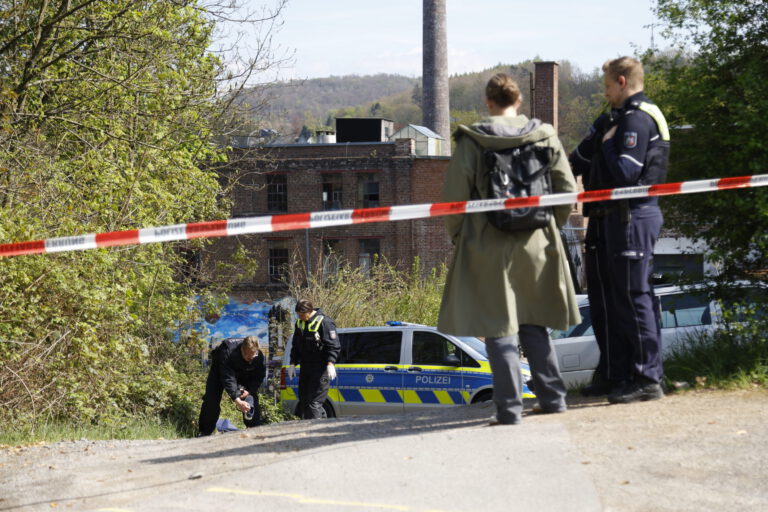Ermittler von der Polizei stehen hinter einer Polizeiabsperrung und untersuchen Spuren auf dem Boden.