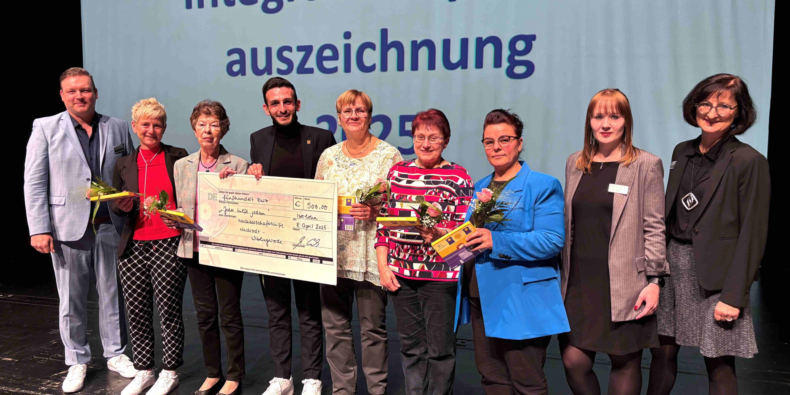 Eine Gruppe Menschen steht nach einer Preisverleihung auf einer Bühne und hält einen 500 Euro Spendenscheck in der Hand.
