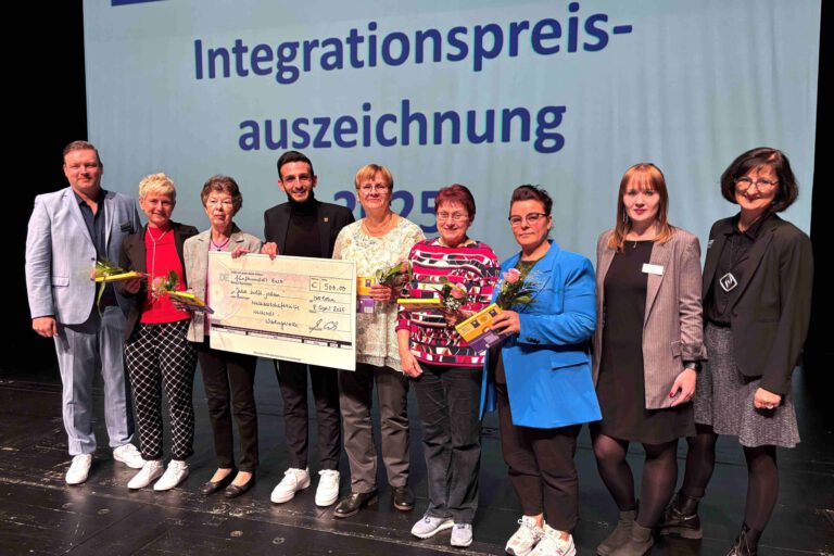 Foto: Märkischer Kreis Eine Gruppe Menschen steht nach einer Preisverleihung auf einer Bühne und hält einen 500 Euro Spendenscheck in der Hand.