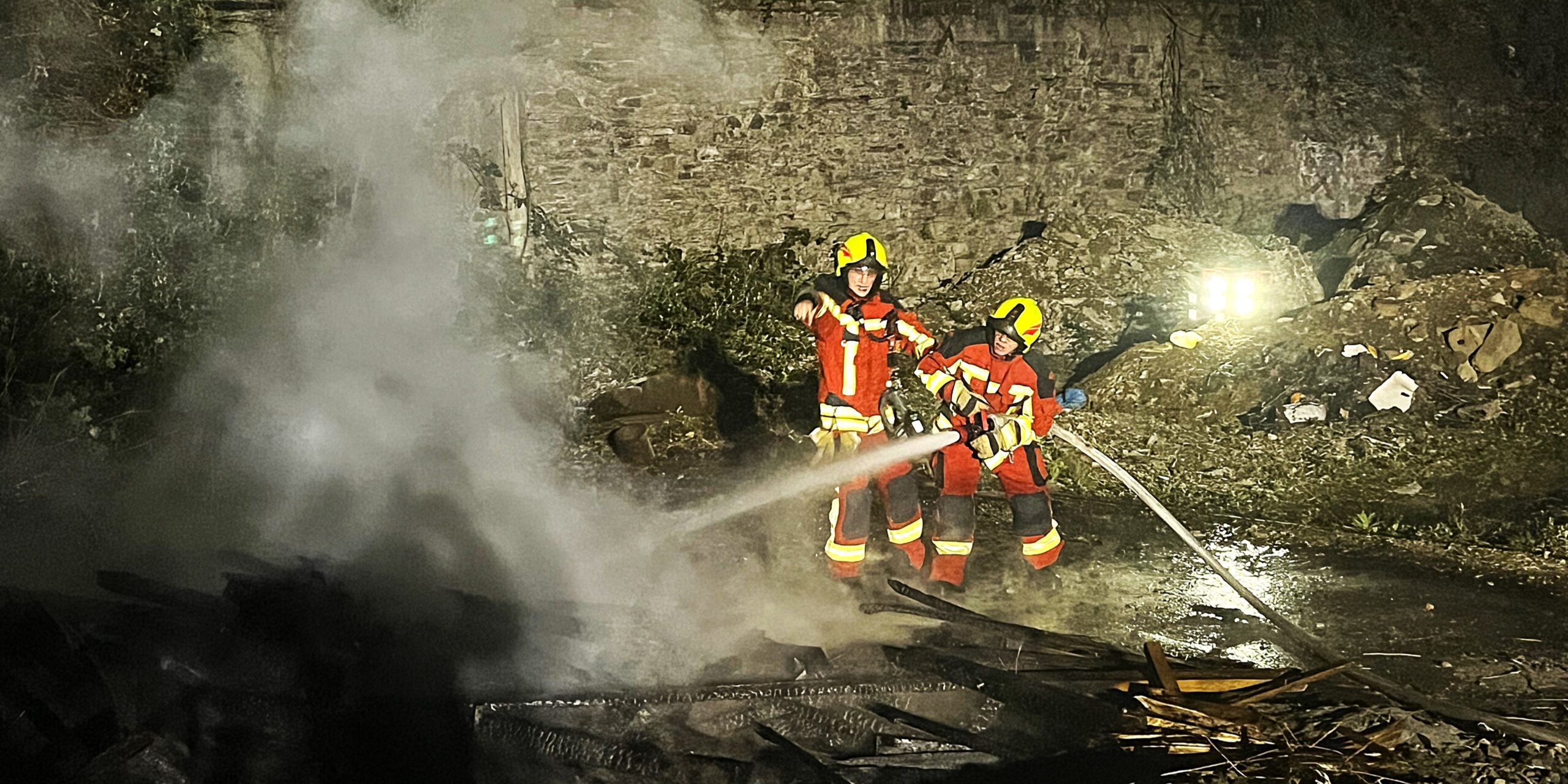 Auf einer Industriebrache löschte die Feuerwehr in der Nacht zu Ostersonntag brennende Holzbretter und Bohlen.
© Foto: Carsten Menzel Zwei Einsatzkräfte der Feuerwehr stehen bei Dunkelheit vor einem brennenden Holzhaufen.