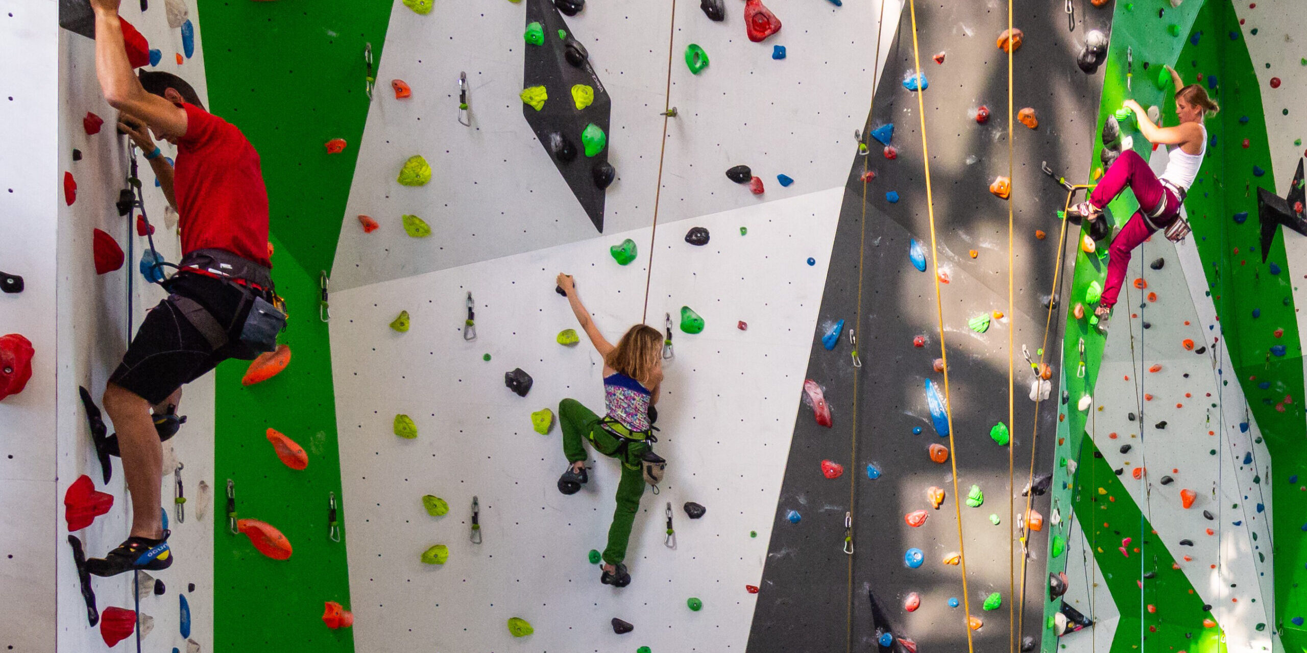 Sich gegenseitig zu unterstützen und sich als Familie mal ganz anders zu erleben, ist beim Klettern und Bouldern möglich - Ein Bildungsplanseminar der Jugendbildungsstätte des Märkischen Kreises.
© Foto: Märkischer Kreis Drei Personen beim Klettern an einer bunten Indoor-Kletterwand mit farbigen Griffen und Sicherungsseilen; ein Kind klettert in der Mitte zwischen zwei Erwachsenen.