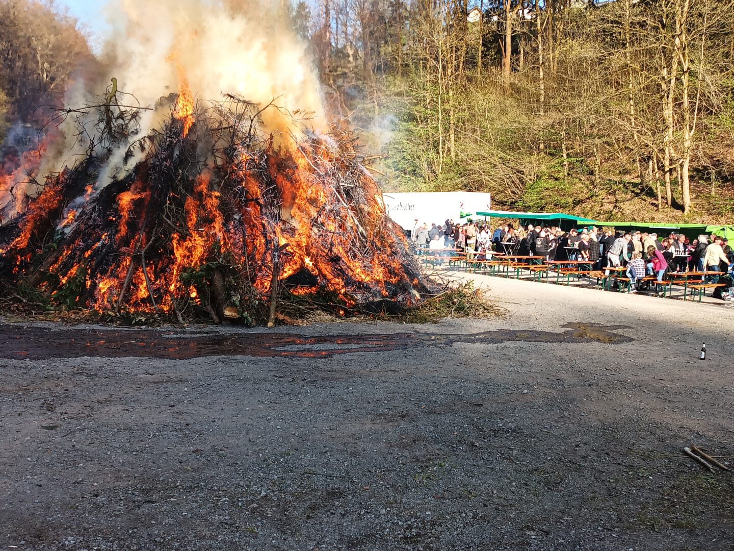 Osterfeuer bei Tageslicht, umgeben von zahlreichen Besuchern.