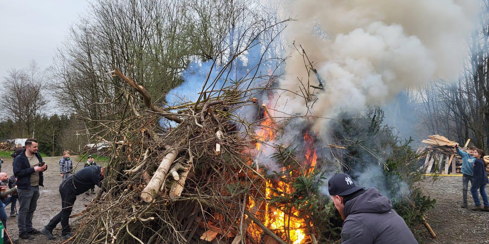 Derzeit besteht die Gefahrenstufe 3 für Waldbrände. Deswegen stehen die geplanten Osterfeuer bis zum 17. April auf der Kippe.
© Archivfoto: Ilka Kremer Osterfeuer mit brennendem Holzhaufen aus Ästen und Baumstämmen, dichter Rauch steigt auf, mehrere Menschen, darunter Kinder, beobachten das Feuer.