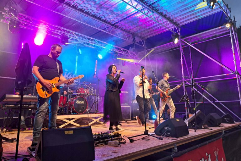 Eine Band performt im Scheinwerferlicht auf einer Bühne.