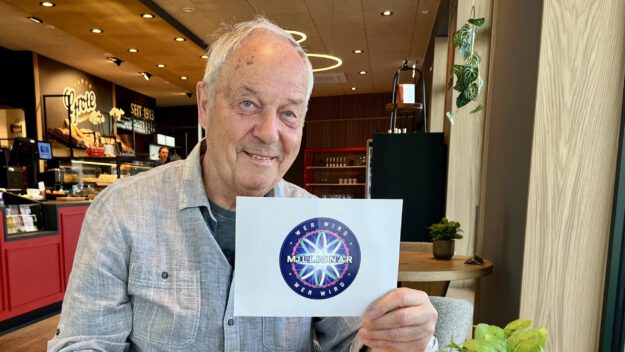 Foto: Carmen Ahlers Wolfhard Köpke sitzt in einem Café und hält eine Moderationskarte von der TV-Sendung "Wer wird Millionär" in der Hand.