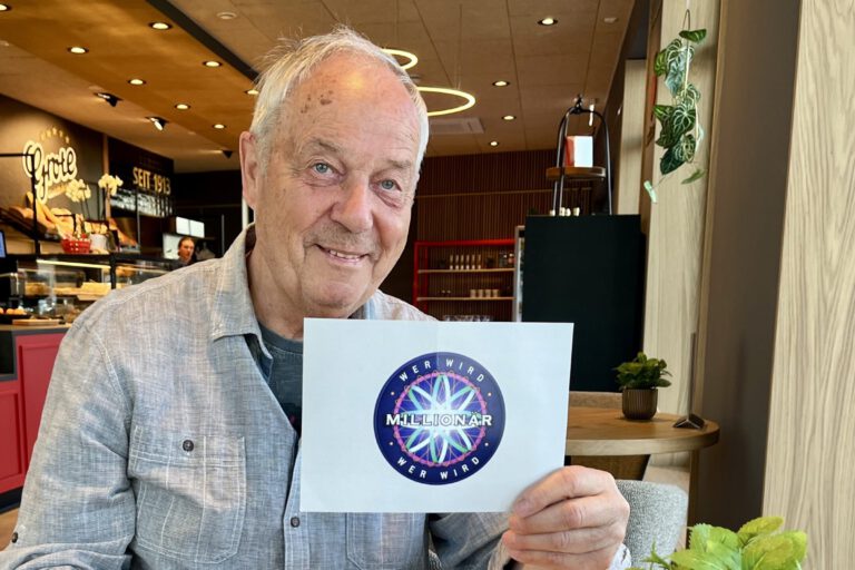 Foto: Carmen Ahlers Wolfhard Köpke sitzt in einem Café und hält eine Moderationskarte von der TV-Sendung "Wer wird Millionär" in der Hand.