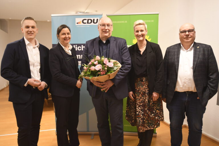 Fünf Personen stehen vor zwei Rollups. Ein Mann hält einen Blumenstrauß.