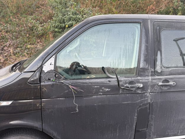 Foto: Kremer Nahaufnahme eines beschädigten schwarzen Autos mit Kratzspuren und Dellen an der linken Fahrzeugseite. Der Außenspiegel ist abgerissen.