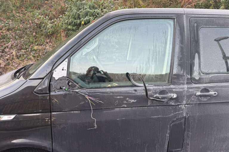 Nahaufnahme eines beschädigten schwarzen Autos mit Kratzspuren und Dellen an der linken Fahrzeugseite. Der Außenspiegel ist abgerissen.