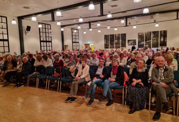 Foto: Freies Theater Auf Draht Altena Zuschauer sitzen in Stuhlreihen in einem beleuchteten Saal.