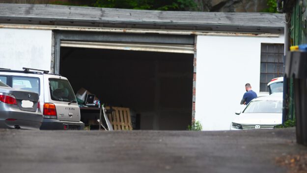 Foto: Carsten Menzel Am Ende einer Einfahrt steht ein weißes Garagengebäude mit geöffnetem Tor. Links stehen daneben zwei Pkw und rechts ein weißer Pkw, auf dessen Beifahrerseite ein Mann in blauem T-Shirt steht.