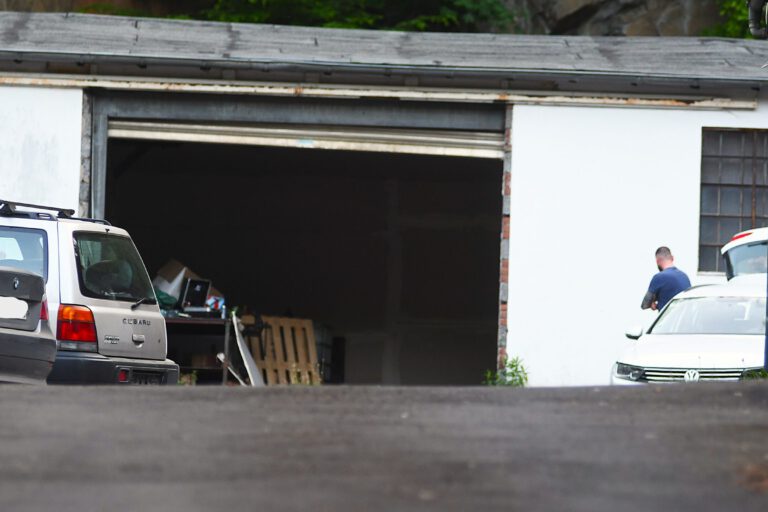 Foto: Carsten Menzel Am Ende einer Einfahrt steht ein weißes Garagengebäude mit geöffnetem Tor. Links stehen daneben zwei Pkw und rechts ein weißer Pkw, auf dessen Beifahrerseite ein Mann in blauem T-Shirt steht.