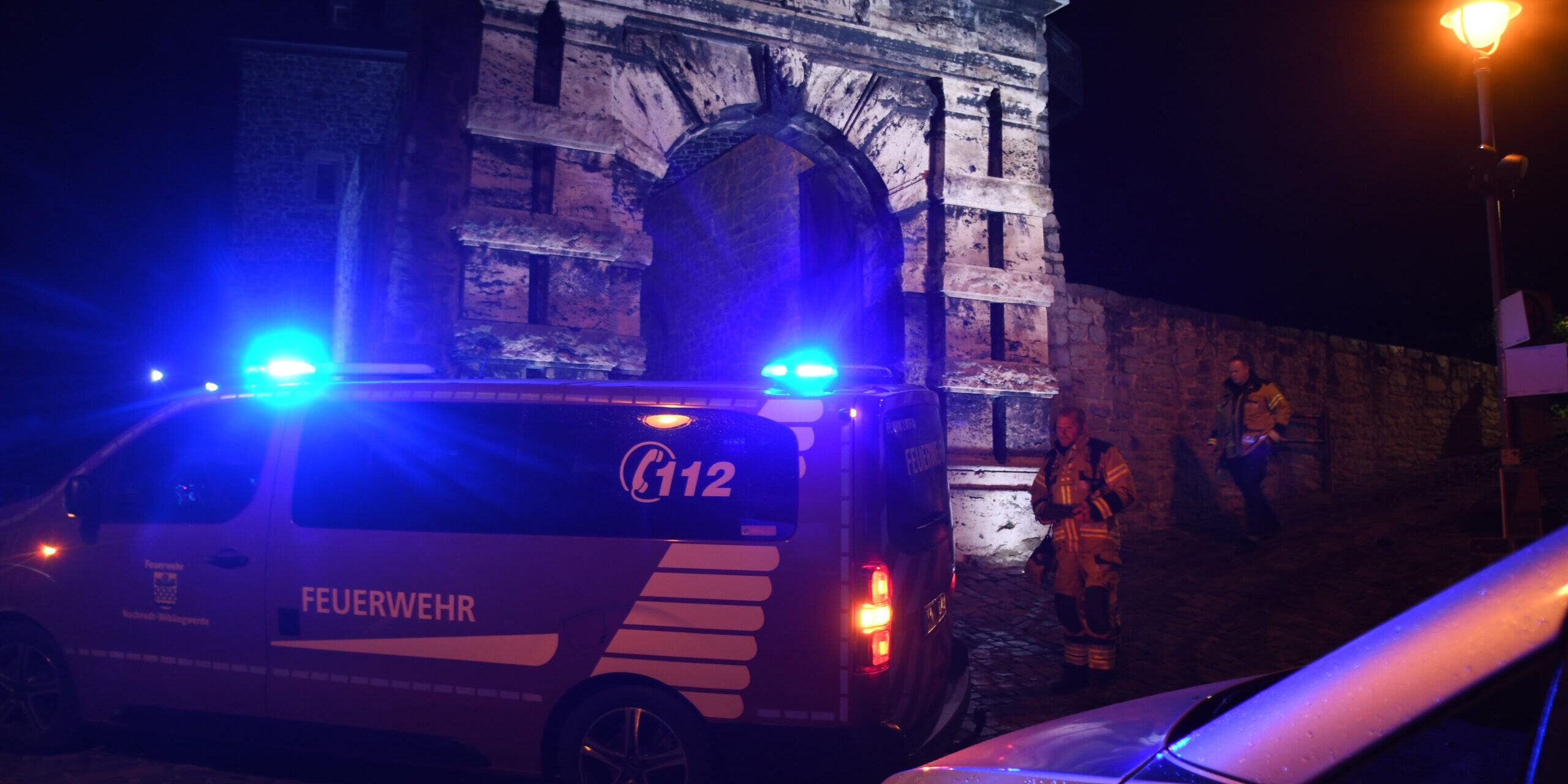 Ein Polizei- und Feuerwehrfahrzeug stehen bei Nacht vor den Burgmauern der Burg Altena.