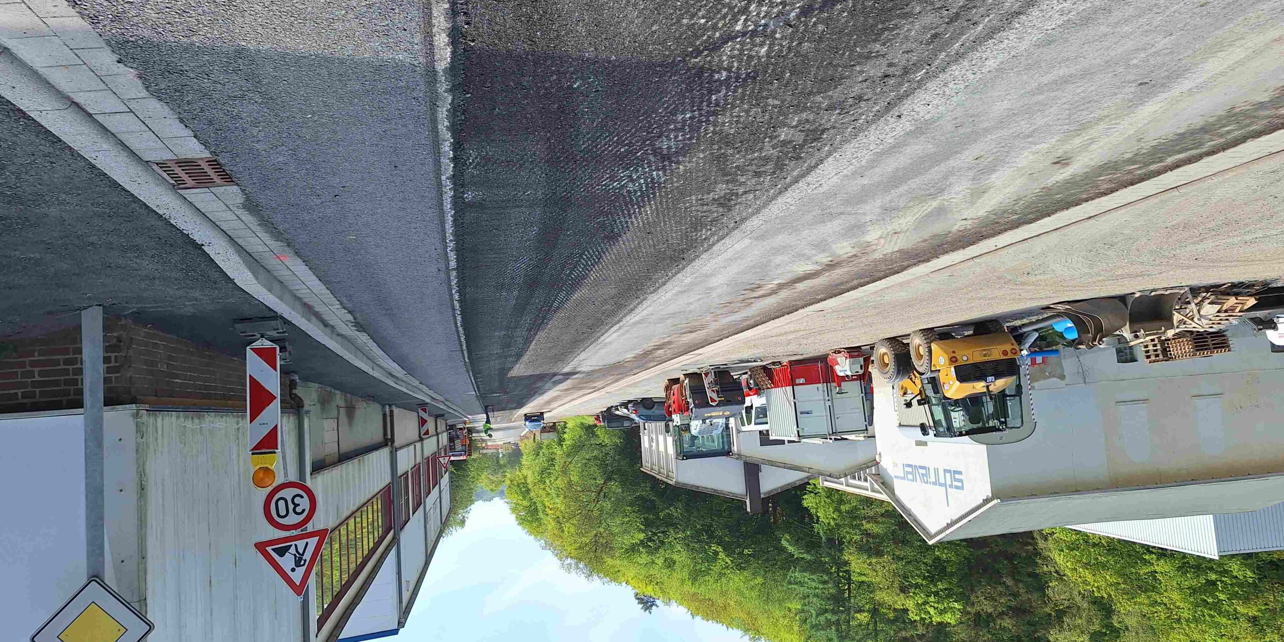 Am Wochenende wird die L698 in Altena auf einem Teilstück asphaltiert. Für diese Maßnahme ist eine Vollsperrung erforderlich. 
© Foto: Maier Baustelle auf einer Straße vor einem Industriegebäude mit mehreren abgestellten Baufahrzeugen und Warnschildern, darunter eine Geschwindigkeitsbegrenzung von 30 km/h.