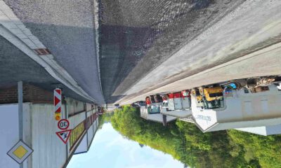Baustelle auf einer Straße vor einem Industriegebäude mit mehreren abgestellten Baufahrzeugen und Warnschildern, darunter eine Geschwindigkeitsbegrenzung von 30 km/h.