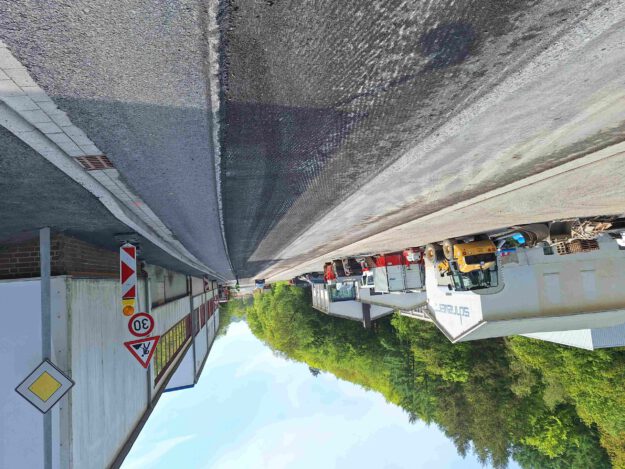 Baustelle auf einer Straße vor einem Industriegebäude mit mehreren abgestellten Baufahrzeugen und Warnschildern, darunter eine Geschwindigkeitsbegrenzung von 30 km/h.