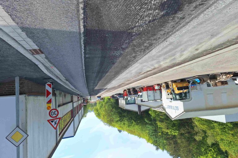 Baustelle auf einer Straße vor einem Industriegebäude mit mehreren abgestellten Baufahrzeugen und Warnschildern, darunter eine Geschwindigkeitsbegrenzung von 30 km/h.