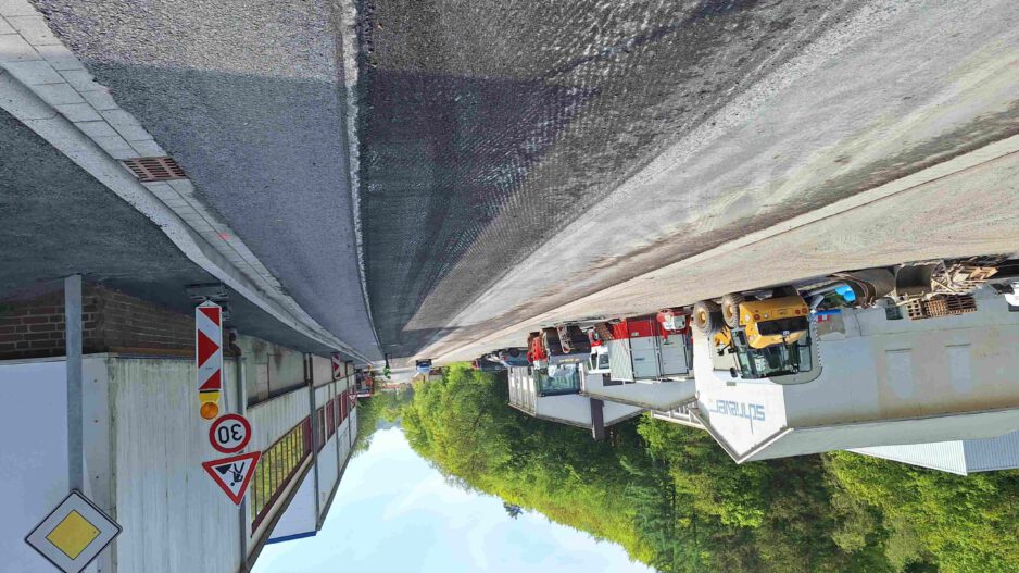 Baustelle auf einer Straße vor einem Industriegebäude mit mehreren abgestellten Baufahrzeugen und Warnschildern, darunter eine Geschwindigkeitsbegrenzung von 30 km/h.